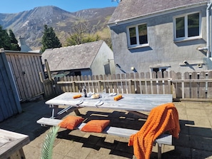 Mesa de madeira posta ao ar livre, com montanhas ao fundo, cerca de madeira e uma casa com fachada cinzenta.