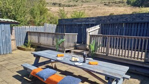 Una terraza de madera con una mesa preparada para dos personas, rodeada por una valla de madera.