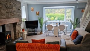 Una sala moderna con chimenea de piedra, televisor de pantalla plana, comedor con mesa y sillas, y un sofá con cojines anaranjados.
