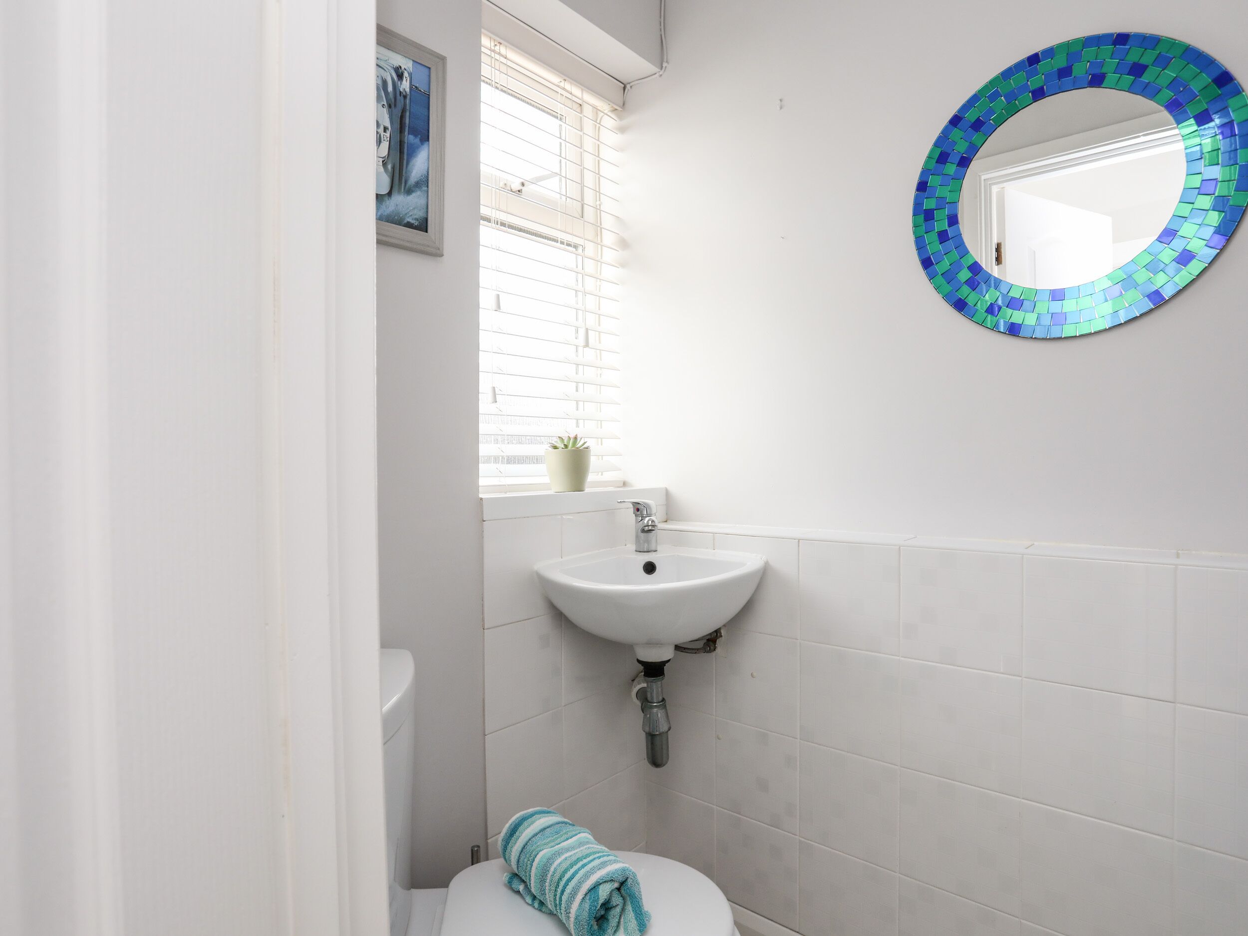 Une salle de bain avec un lavabo blanc, des toilettes et une fenêtre avec des stores.