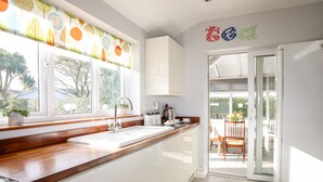 A modern kitchen with a wooden countertop, white cabinets, and a large window. - Bryngwyn - Trearddur Bay (Holyhead)