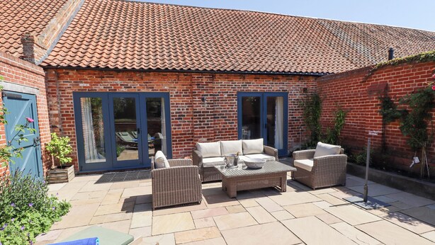 A brick building with a tiled roof, a patio with wicker furniture, and a blue door.