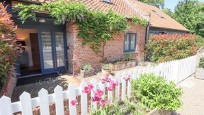 A brick house with a tiled roof, a white picket fence, and a garden with pink flowers.