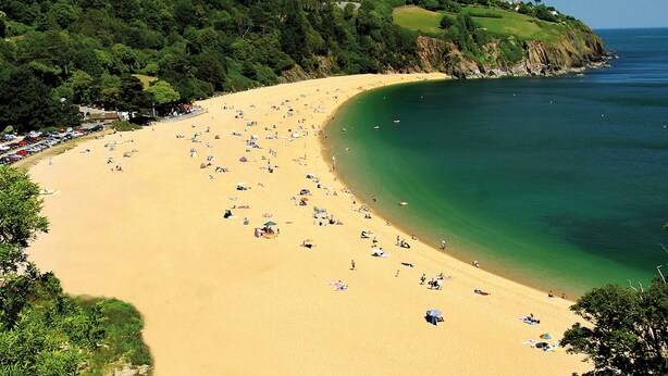 A wide sandy beach with clear green waters, surrounded by lush greenery and hills. - 2 Sails (Dartmouth)