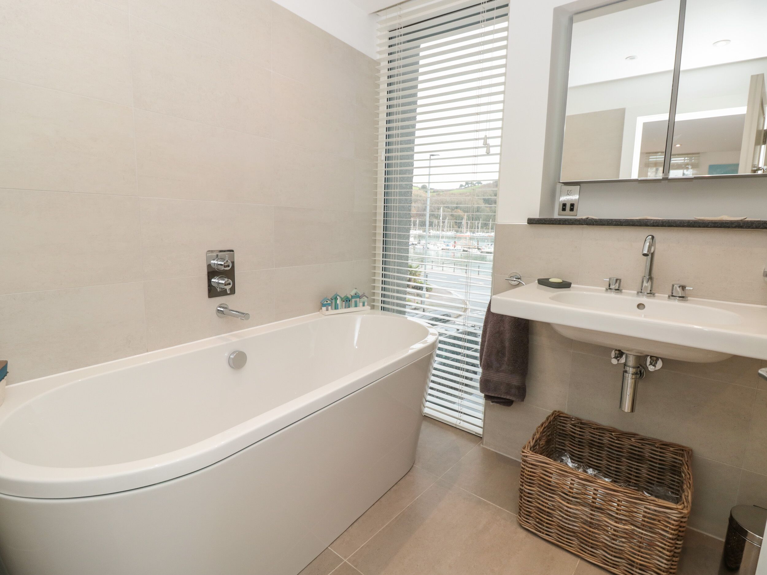 Un baño moderno con bañera, lavamanos y ventana con persianas.