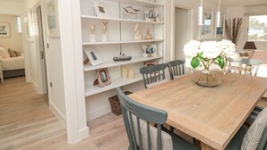 A dining area with a wooden table, chairs, and a white shelving unit with decorative items. - 2 Sails (Dartmouth)