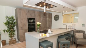 A modern kitchen with a central island, bar stools, a clock, and a potted plant. - 2 Sails (Dartmouth)