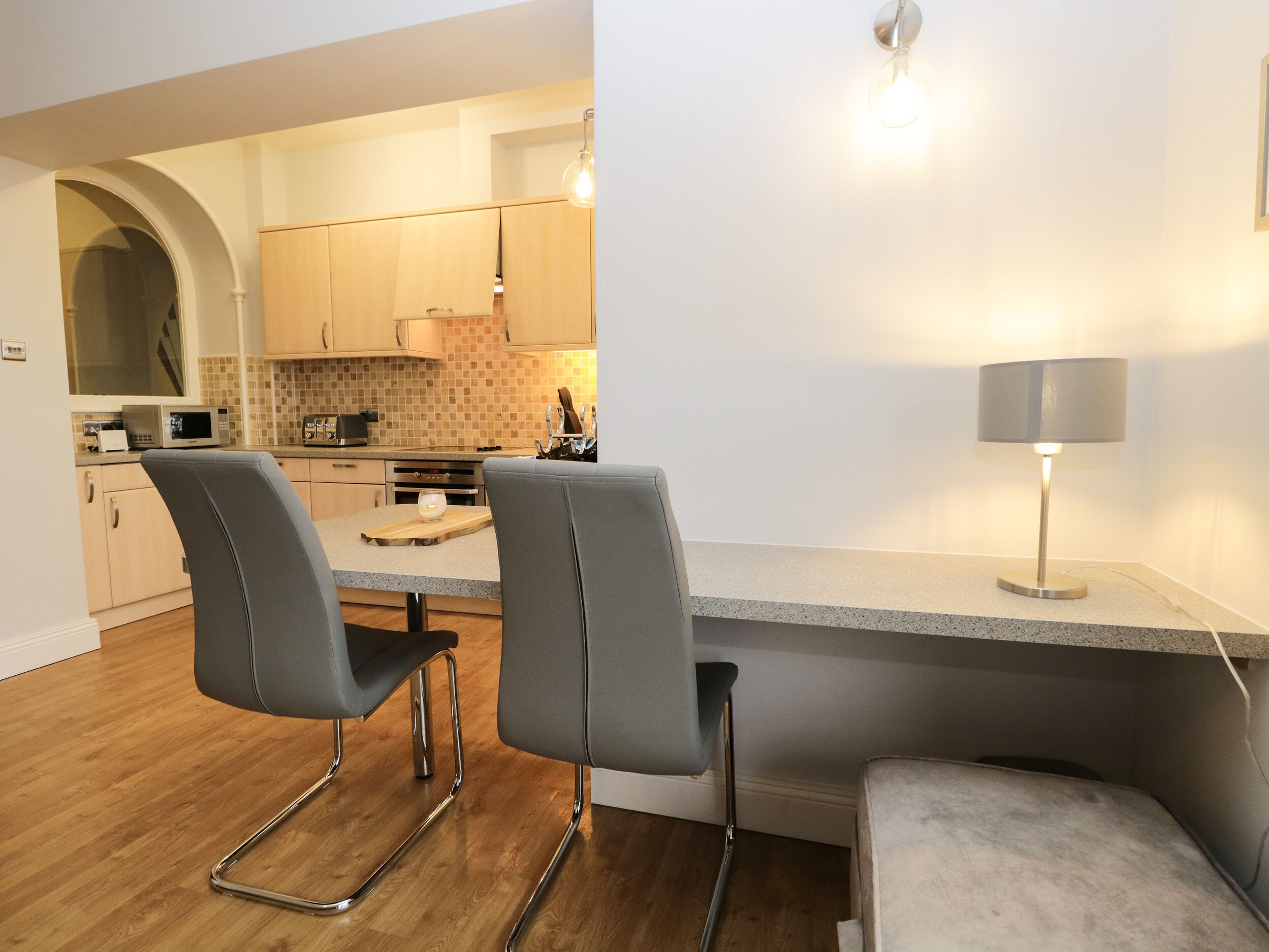 A modern kitchen with two grey chairs, a wooden countertop, and a lamp.