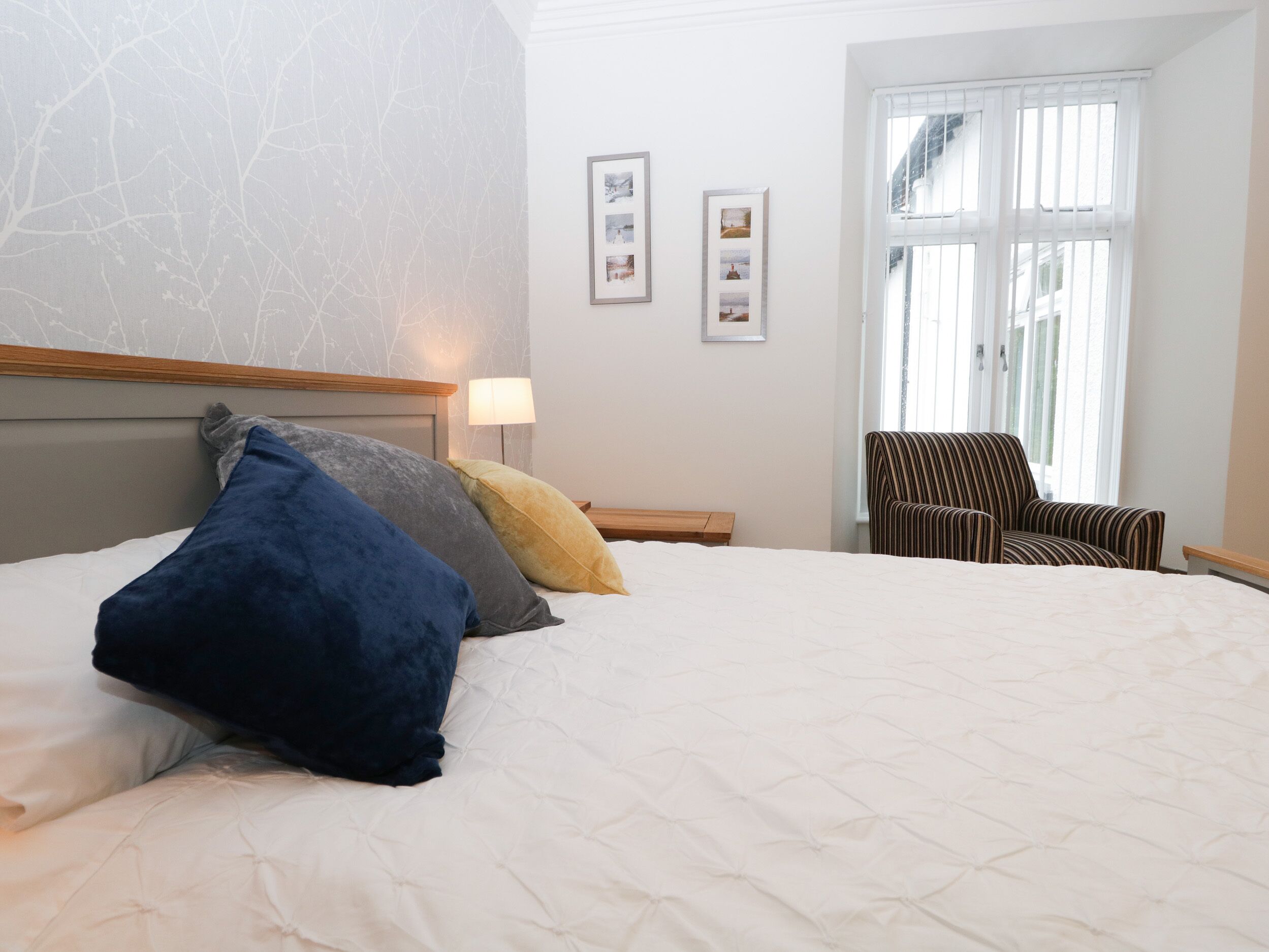 A hotel room with a large bed, a chair, and a window with blinds.