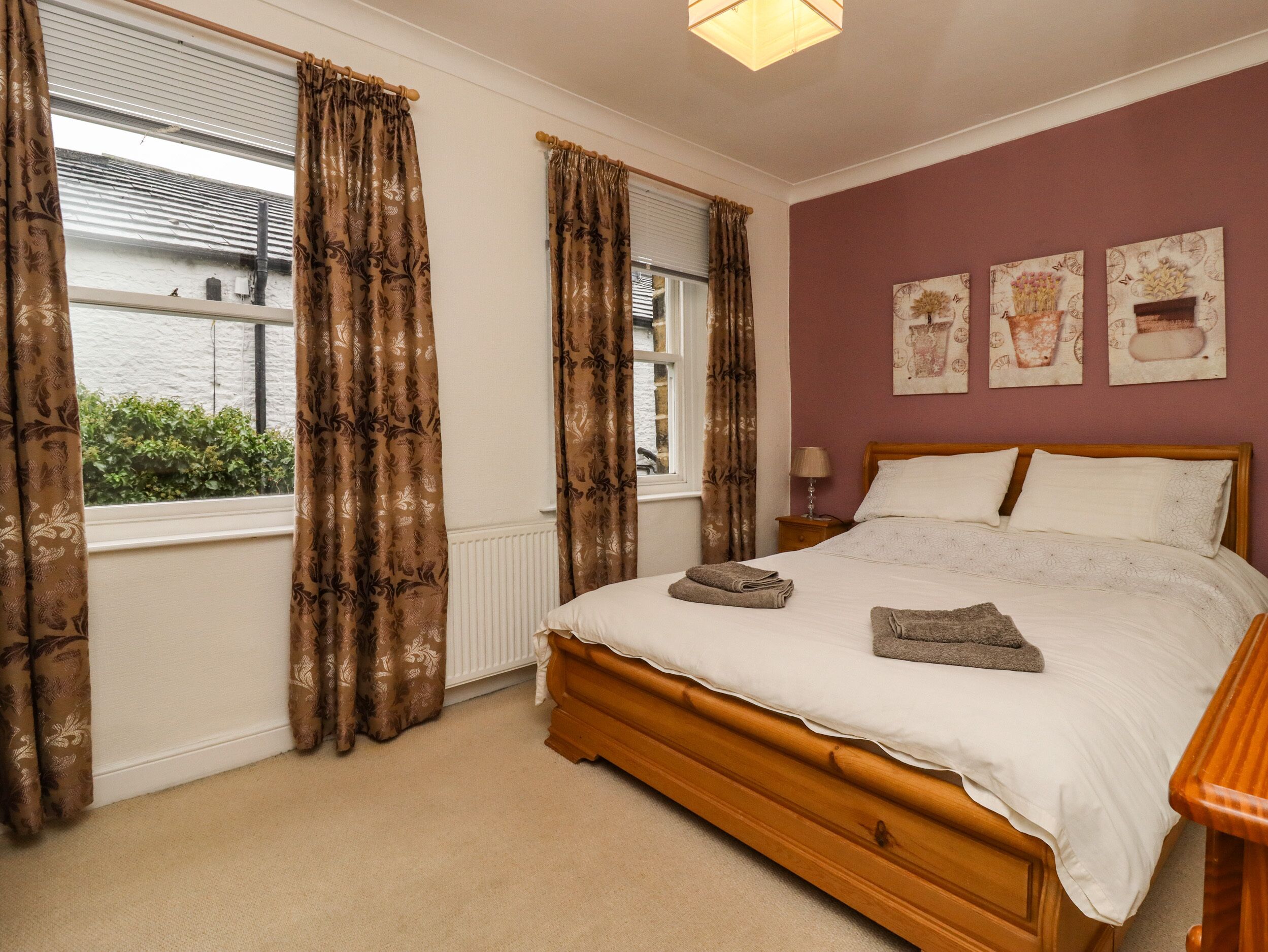A bedroom with a wooden bed, beige curtains, and a view of greenery outside.