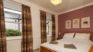 Un dormitorio con cama de madera, cortinas color beige y vista a zonas verdes.