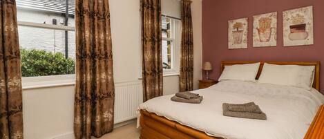 A bedroom with a wooden bed, beige curtains, and a view of greenery outside.