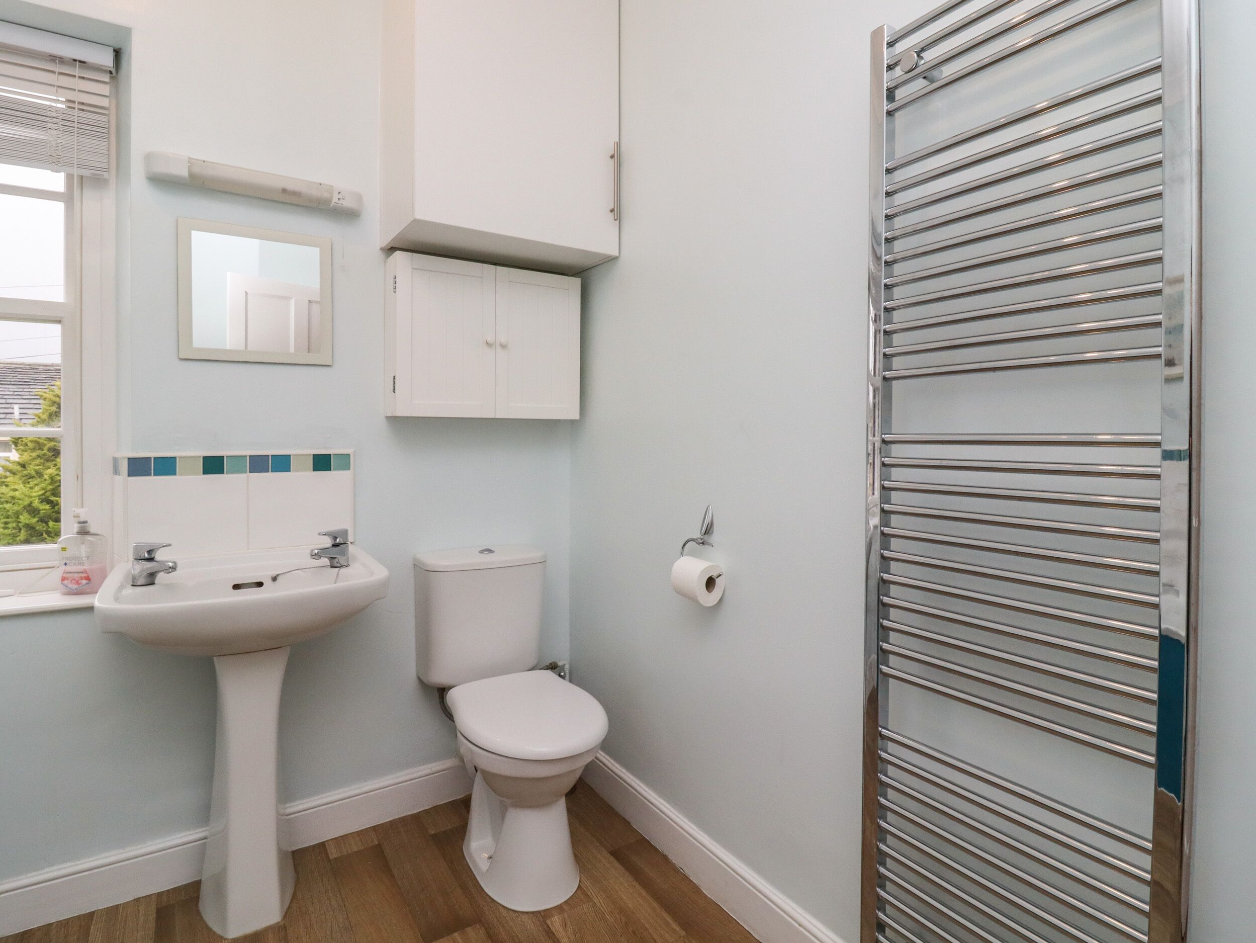 A bathroom with a white sink, toilet, and cabinet, a mirror, and a towel rack.