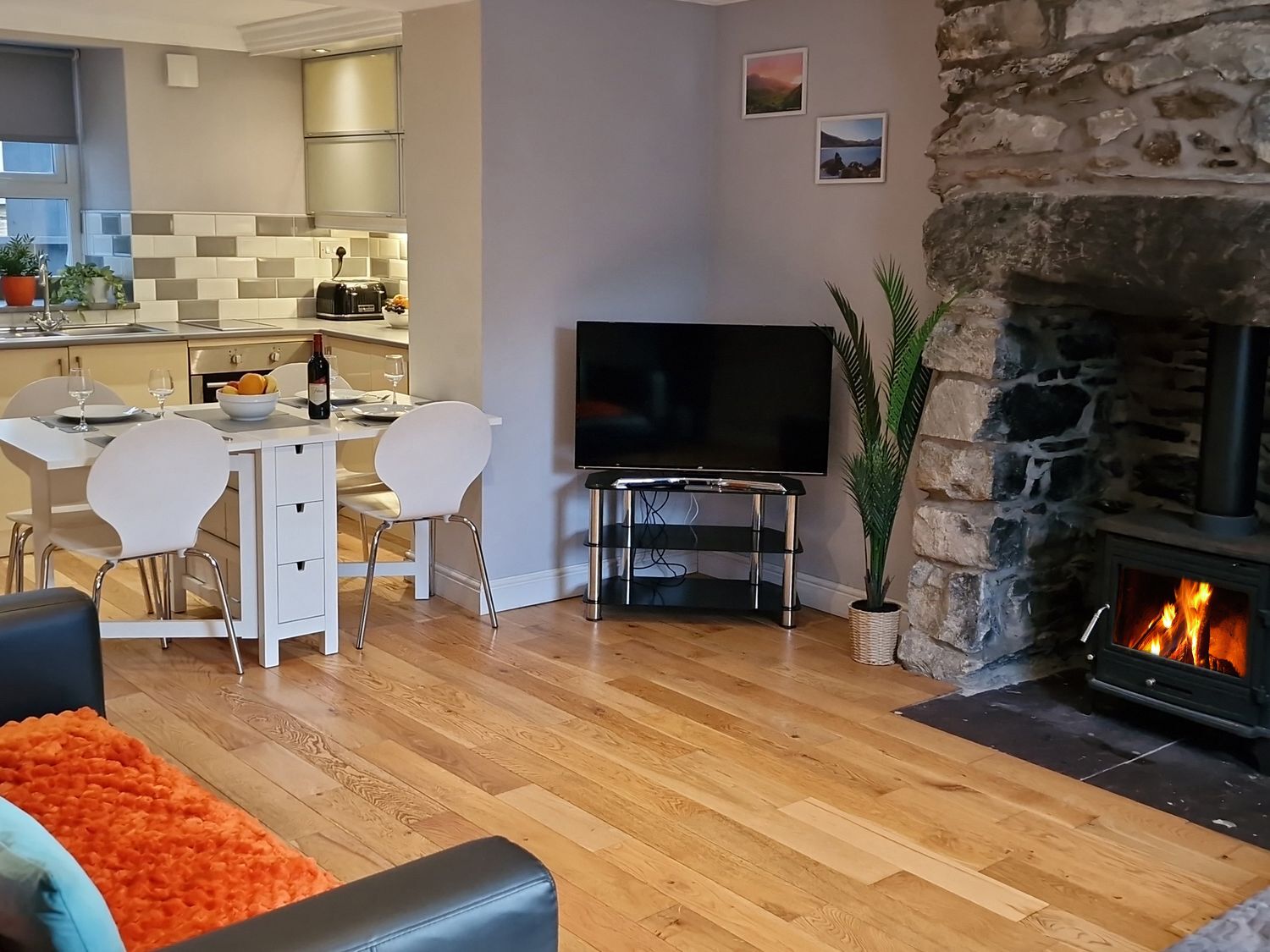 Un salon moderne avec une cheminée en pierre, un coin repas avec une cuisine en arrière-plan et un téléviseur à écran plat.