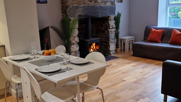 Comedor con chimenea de piedra, sillas blancas y una mesa dispuesta para dos.