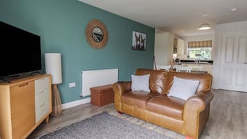 Una sala de estar con un sofá de cuero marrón, un aparador de madera, un televisor y un espejo montado en la pared.
