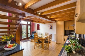 A modern kitchen with wooden beams, a dining area with a table and chairs, and a view of the outdoors. - Nest Barn (Keswick)