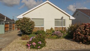 Een gelijkvloers huis met schuin dak, een stenen fundering en een voortuin met diverse bloeiende planten en struiken.