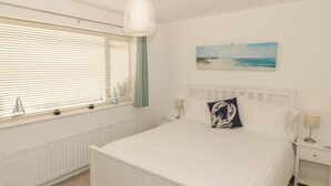 Een slaapkamer met een groot bed, een raam met zonwering, een radiator, een nachtkastje met een lamp en een schilderij aan de muur.