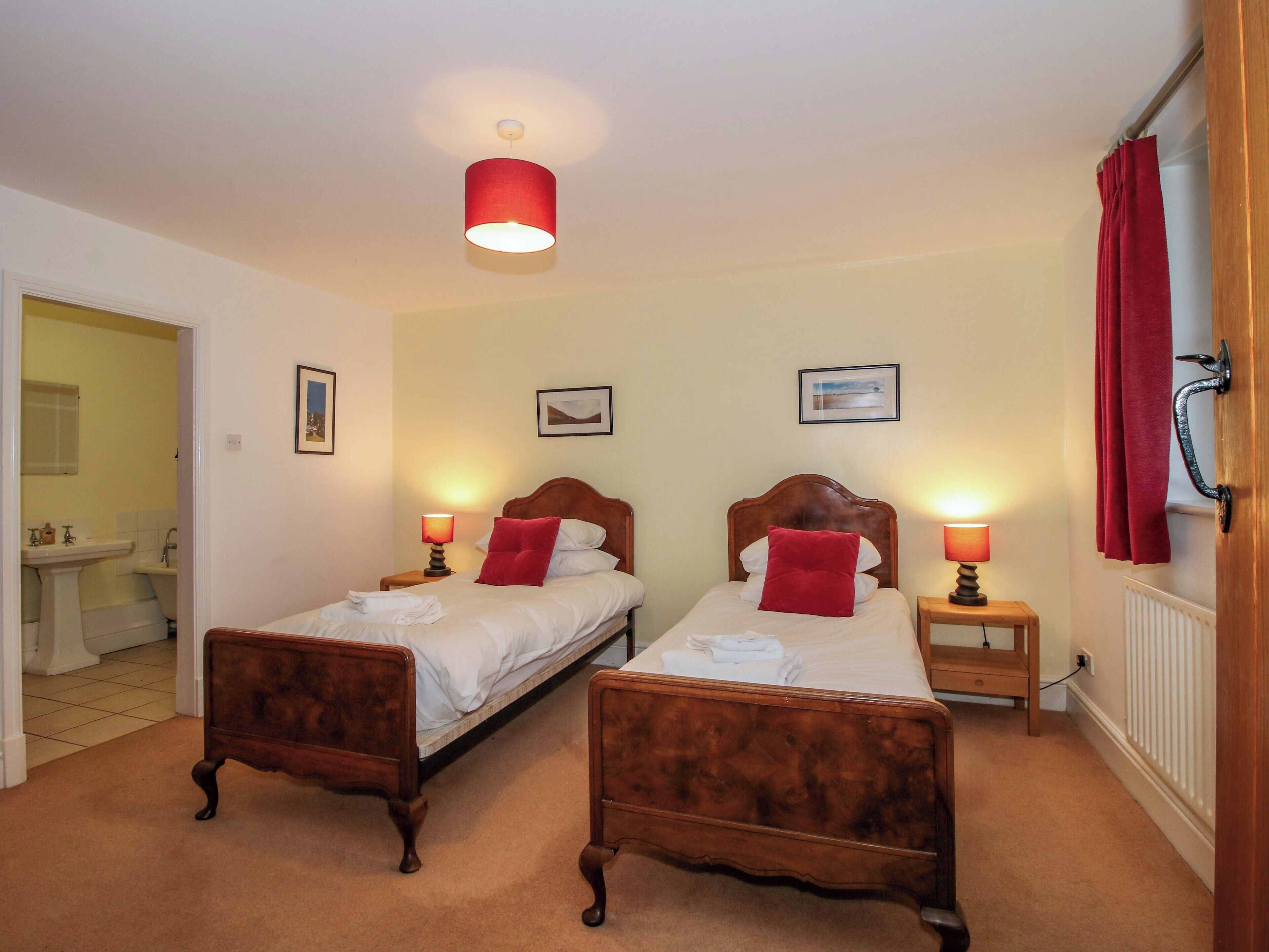 A bedroom with two wooden beds, each with a red pillow and a bedside table with a lamp.