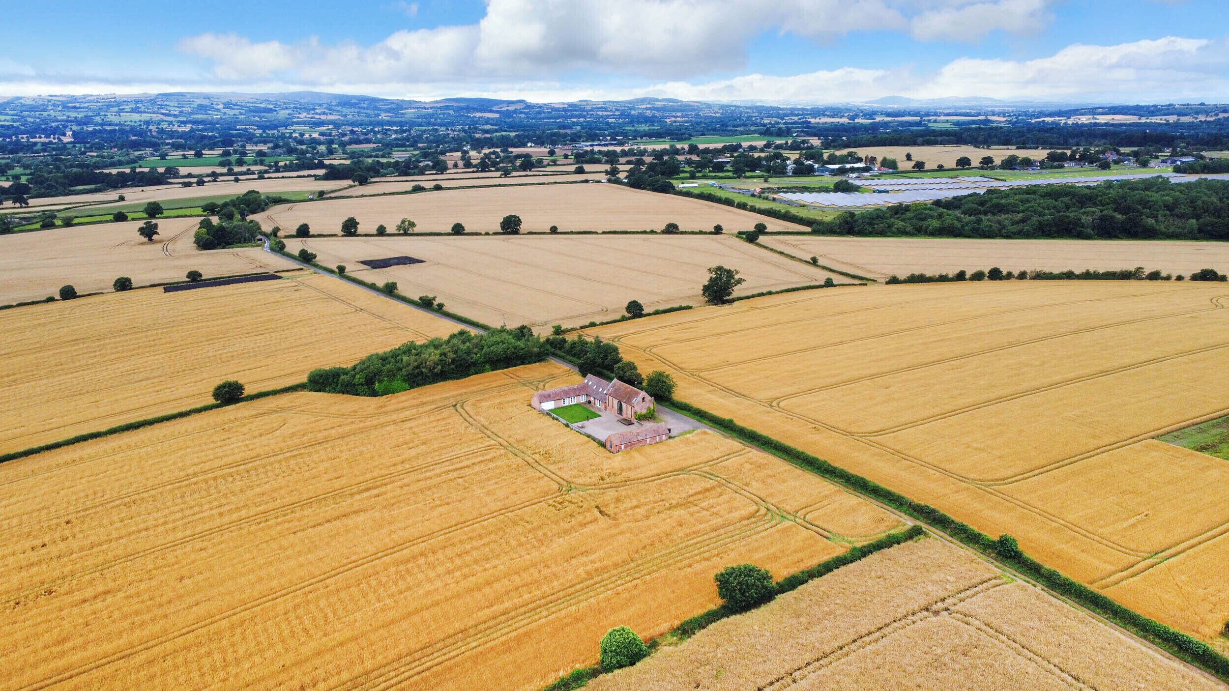 An aerial view of a rural landscape with fields, a small building, and distant hills.