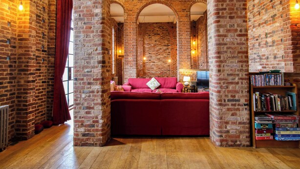 A cozy room with exposed brick walls, a red sofa, and a bookshelf filled with books. - Windy Mundy Farm at Pitchford Estate (Shrewsbury)