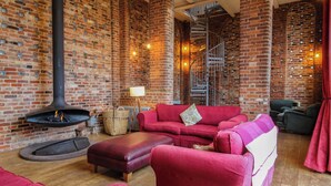 A cozy room with a brick wall, a fireplace, a red sofa, and a spiral staircase. - Windy Mundy Farm at Pitchford Estate (Shrewsbury)