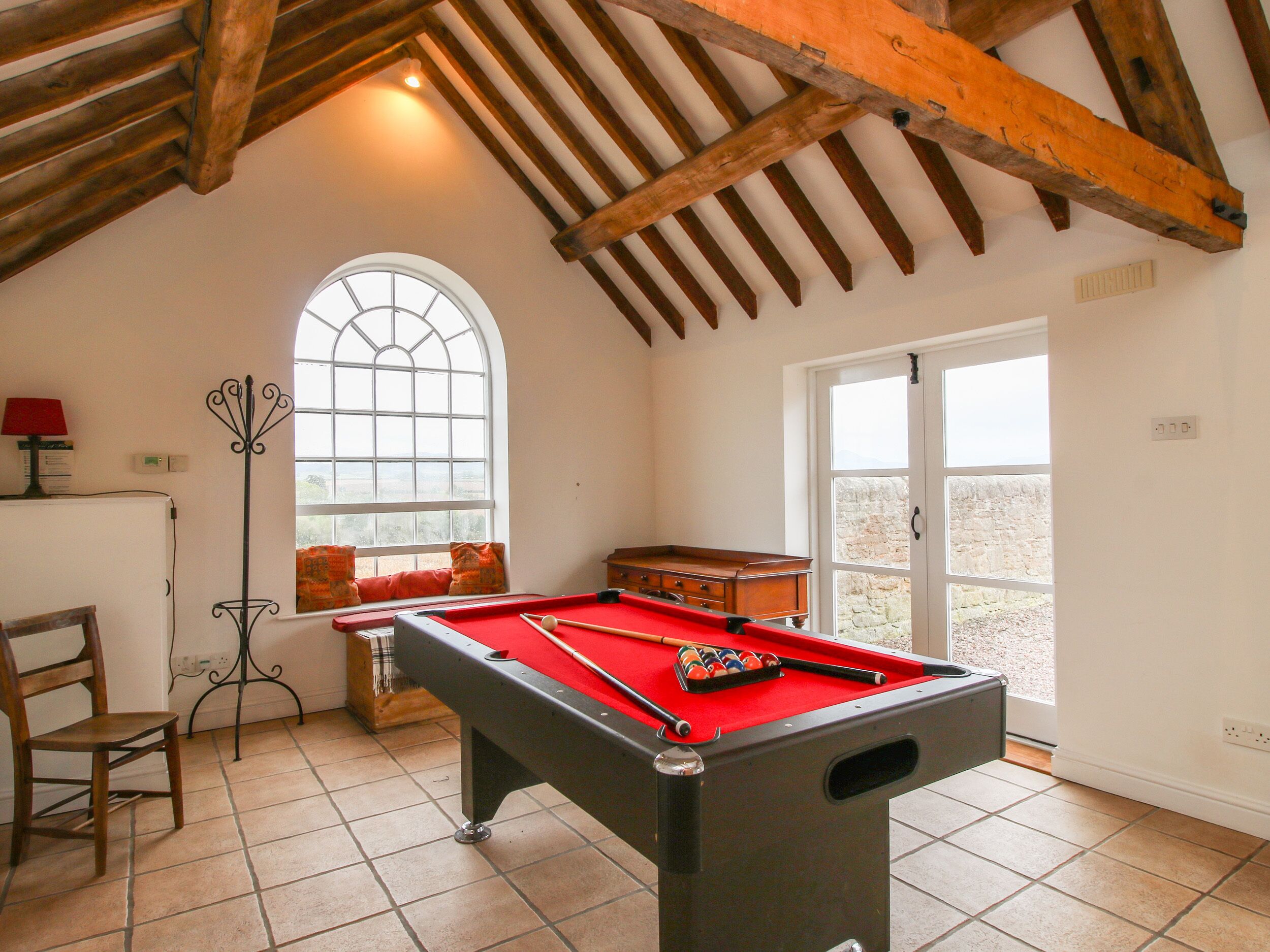 Une table de billard dans une pièce avec un plafond haut, une fenêtre et une porte donnant sur l’extérieur.