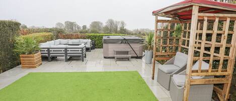 A patio area with a hot tub, outdoor furniture, and a wooden pergola.