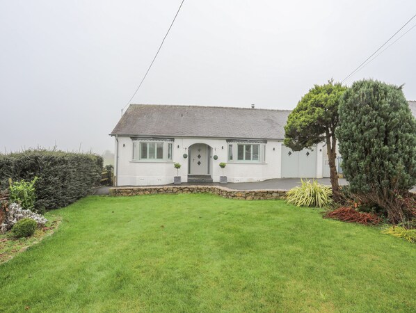 A white house with a grey roof, a front door, and a small front garden.