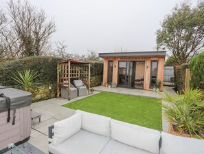 Un espace de vie extérieur moderne, doté d’un coin salon abrité, d’une petite structure en bois et d’une pelouse bien entretenue.