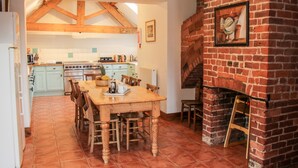 Une cuisine avec une table en bois, des chaises, une cheminée en briques et un sol carrelé.