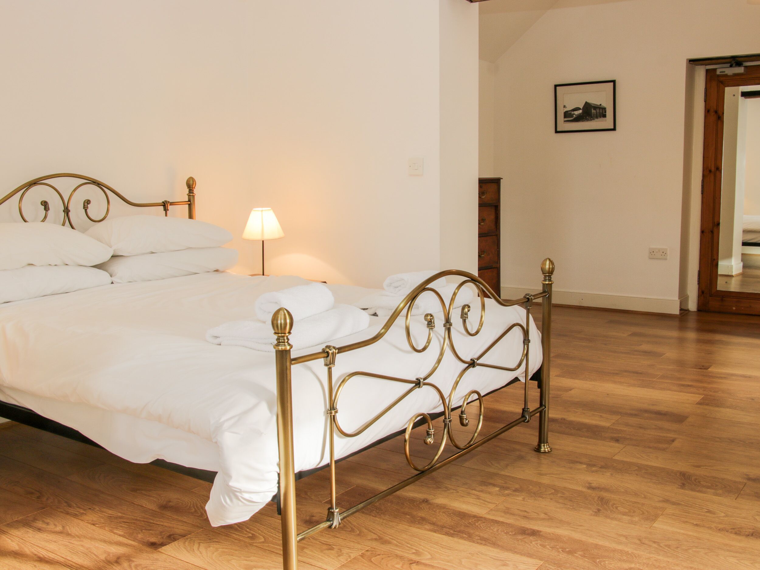 A neatly made bed with white linens and a gold metal frame in a room with wooden flooring.