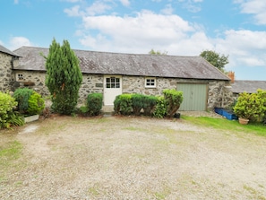 Une maison en pierre avec une allée en gravier, une porte verte et une petite fenêtre.