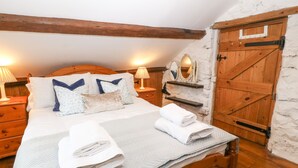 Ein Schlafzimmer mit einem hölzernen Bett, weißer Bettwäsche, einem Nachttisch aus Holz mit Lampe, einem Holzschrank und einer Wand in Weiß mit rustikaler Struktur.