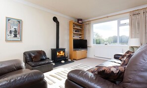 A living room with a fireplace, leather sofas, a television, and a window with curtains. - Honister Cottage (Ambleside)