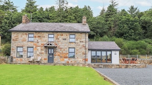 A stone house with a front door, multiple windows, and a small attached structure with a glass door.