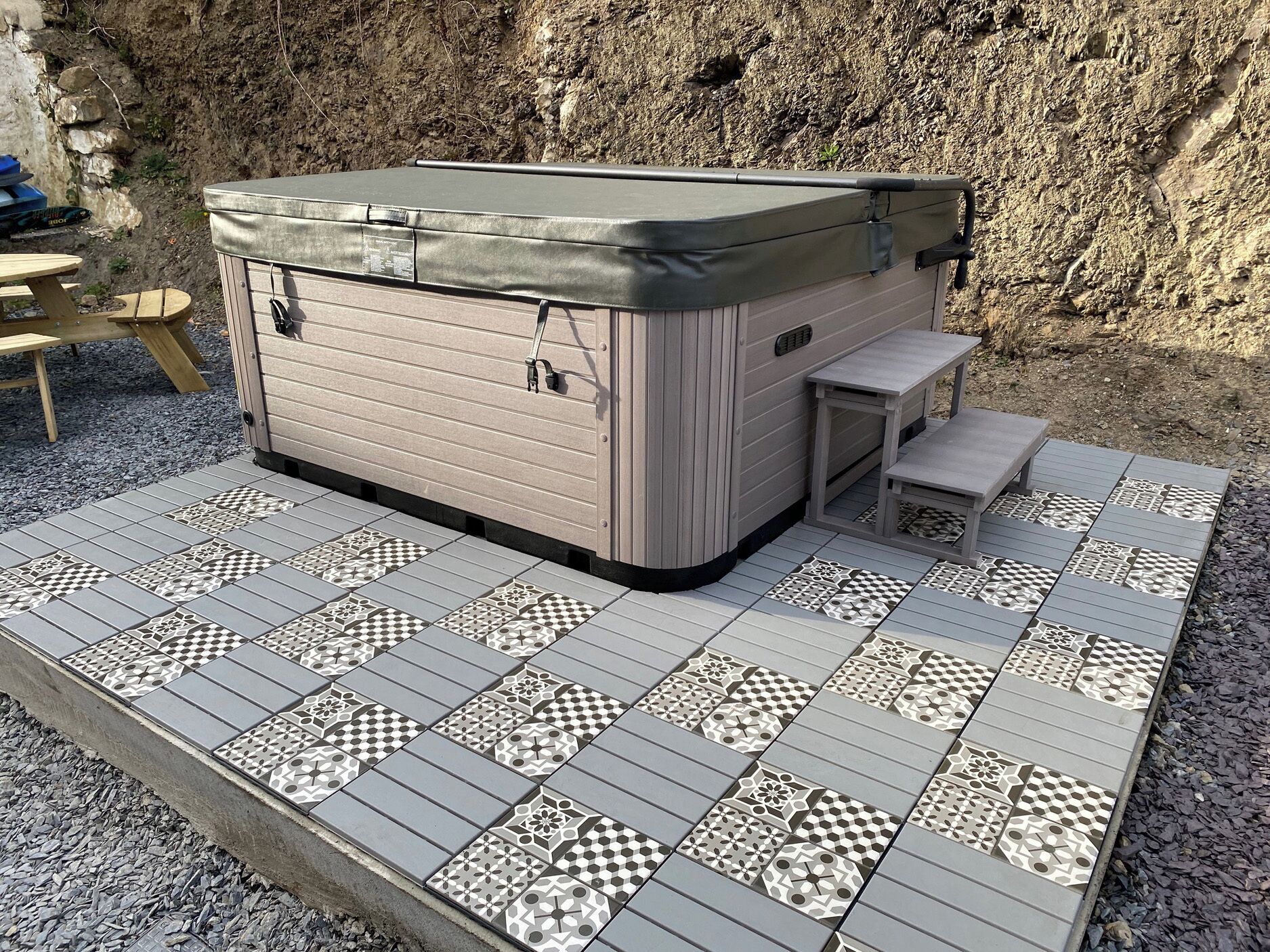A hot tub with a cover, a small table, and a bench.