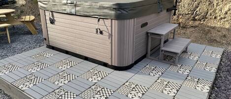 A hot tub with a cover, a small table, and a bench.