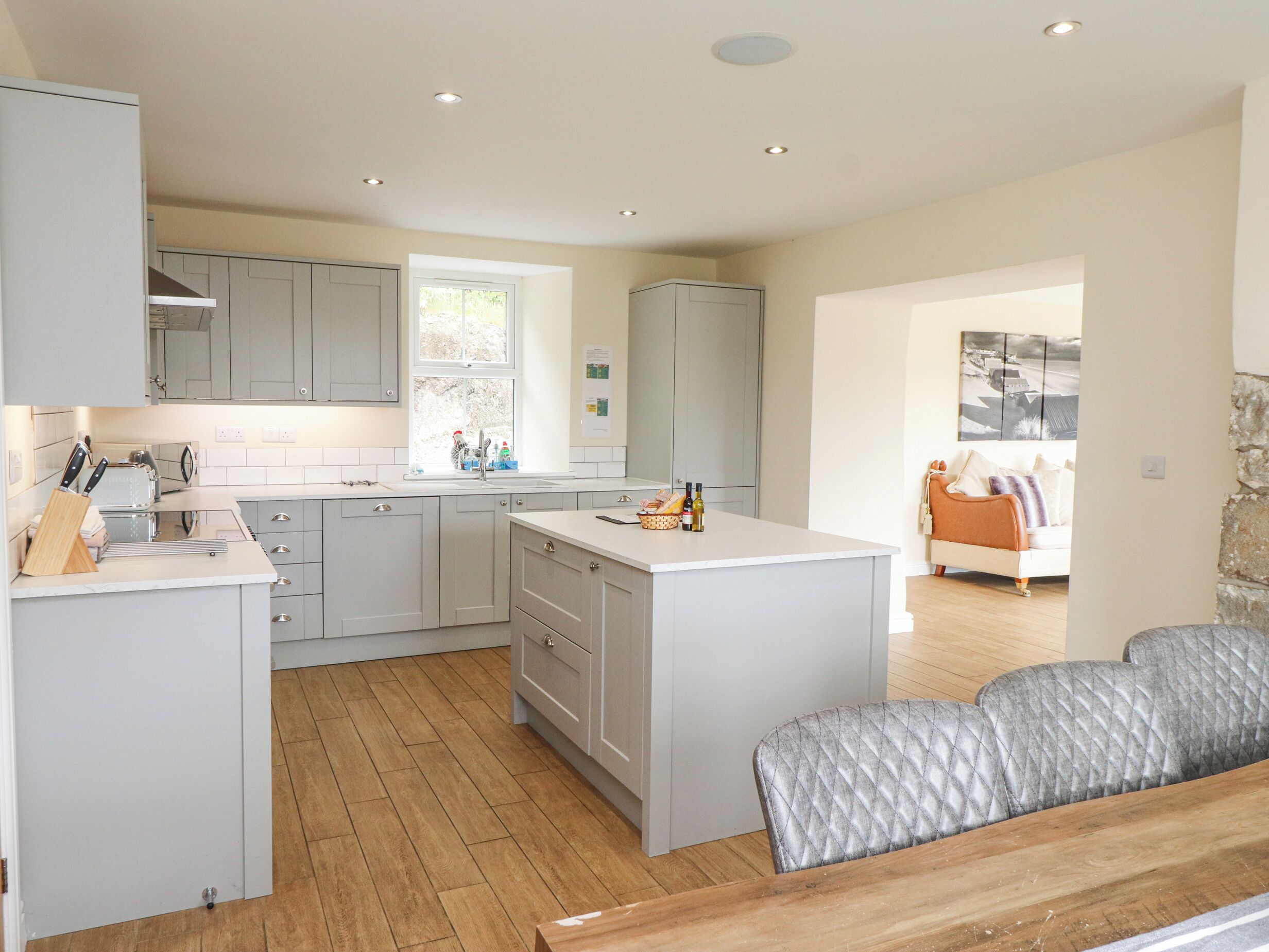 A modern kitchen with grey cabinets, a central island, and a dining area with a grey upholstered sofa.