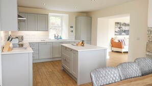 A modern kitchen with grey cabinets, a central island, and a dining area with a grey upholstered sofa.