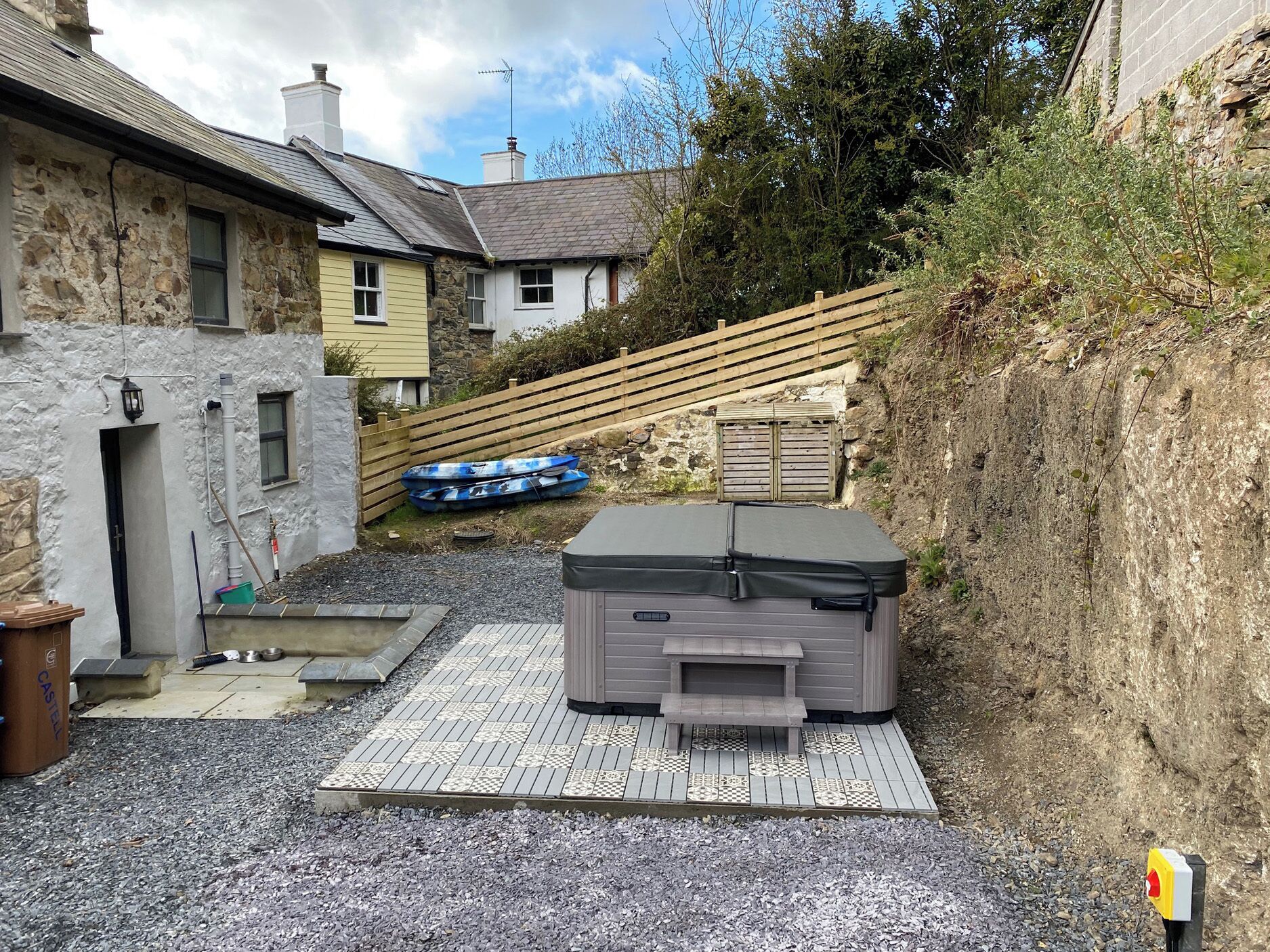 A courtyard with a hot tub, a wooden deck, and a stone wall.