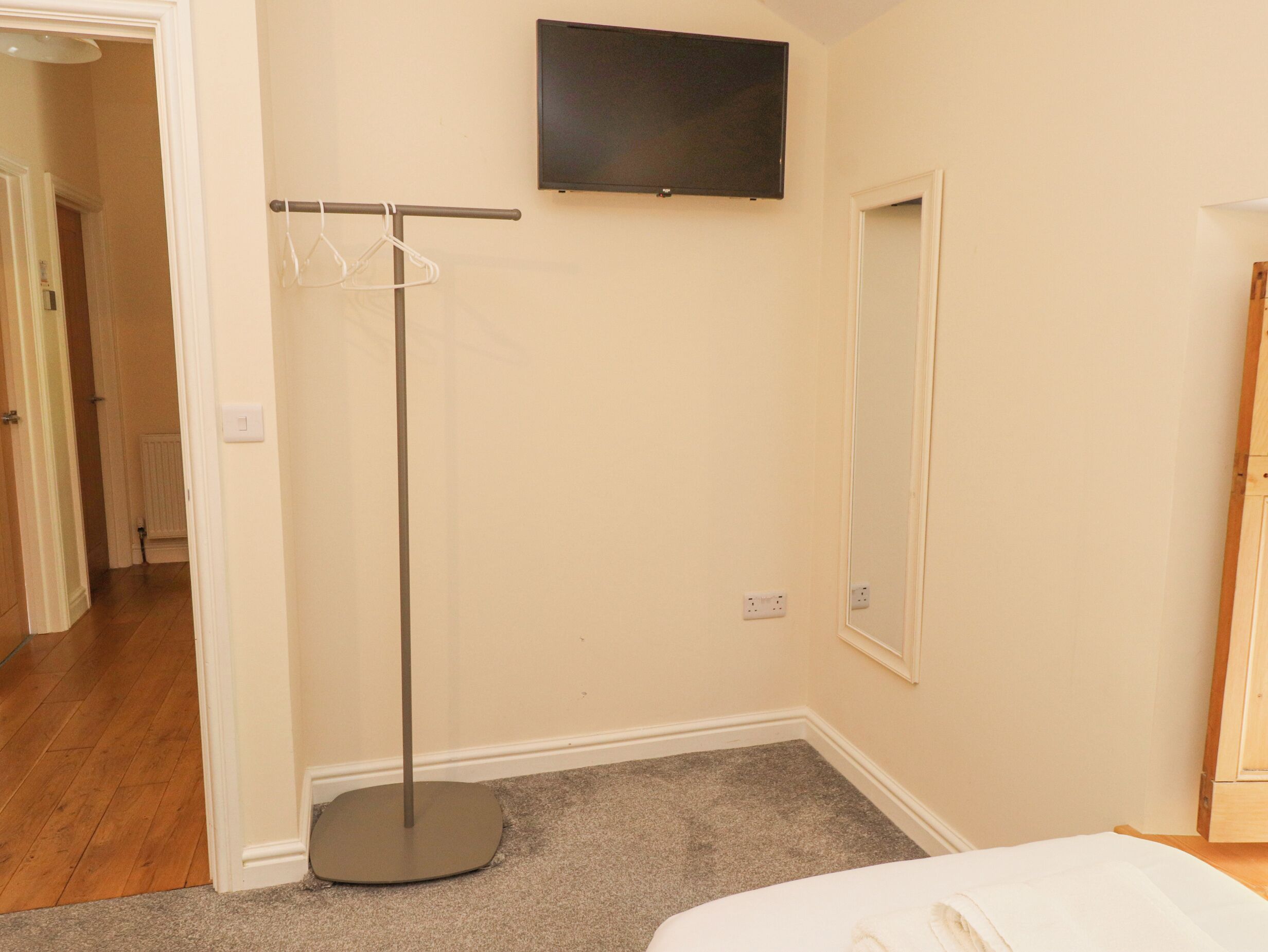Quarto com cama, televisão na parede, cabideiro e espelho.