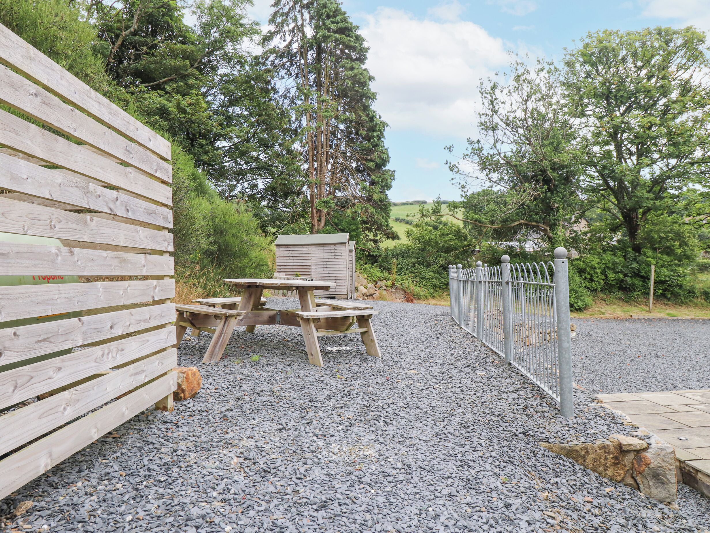 A wooden fence, a picnic table, and a small shed in a garden area with gravel ground.
