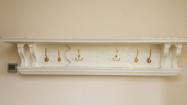 A white wall-mounted coat rack with six hooks. - The Cottage (Pwllheli)