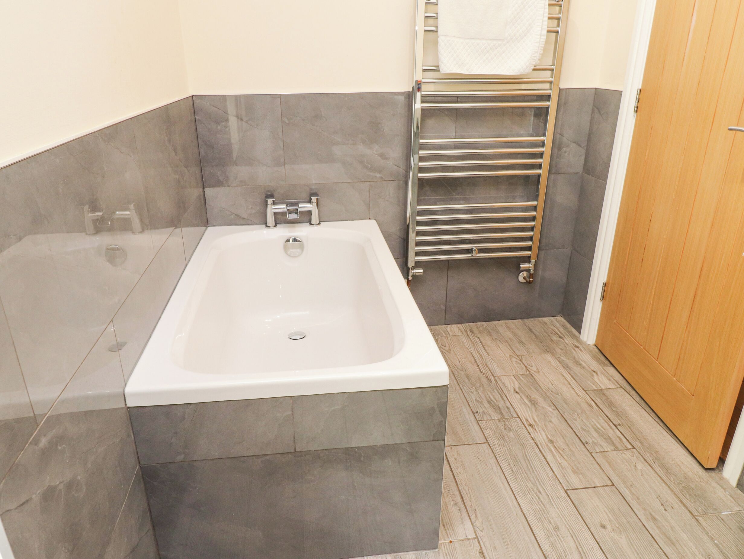 A bathroom with a bathtub, a towel rack, and a wooden floor.