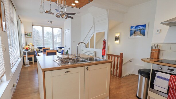 A modern kitchen with a central island, wooden flooring, and a dining area in the background. - Windows (Ambleside)