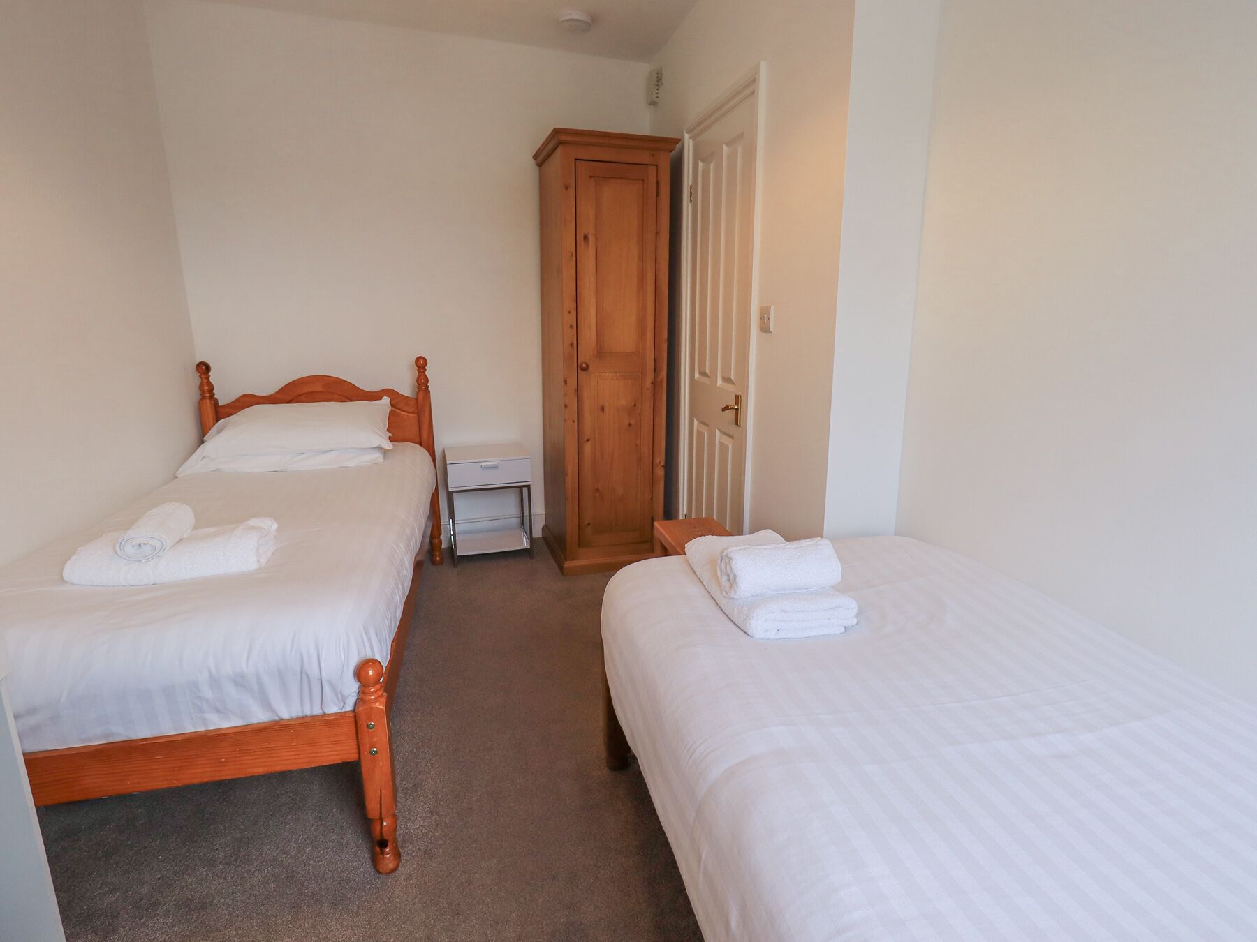 A hotel room with two single beds, a wooden wardrobe, a bedside table, and a door.