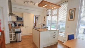 A modern kitchen with white cabinetry, a central island, and a dining area with a wooden table. - Windows (Ambleside)