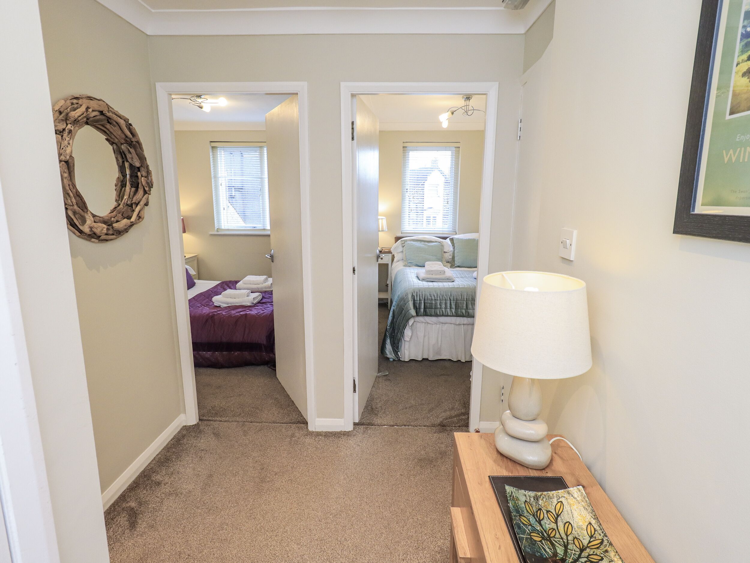 A hallway leading to a bedroom with a bed, a nightstand, a lamp, and a framed picture on the wall.